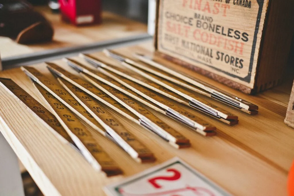 Eine Sammlung von Holzlinealen auf einem Regalbrett.